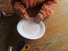 Ein Kind bemalt einen Pappteller orange