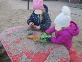 Zwei Kinder backen mit Sand einen Kuchen